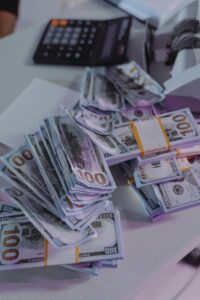 A close-up view of stacked US dollar bills next to a calculator and money counter.