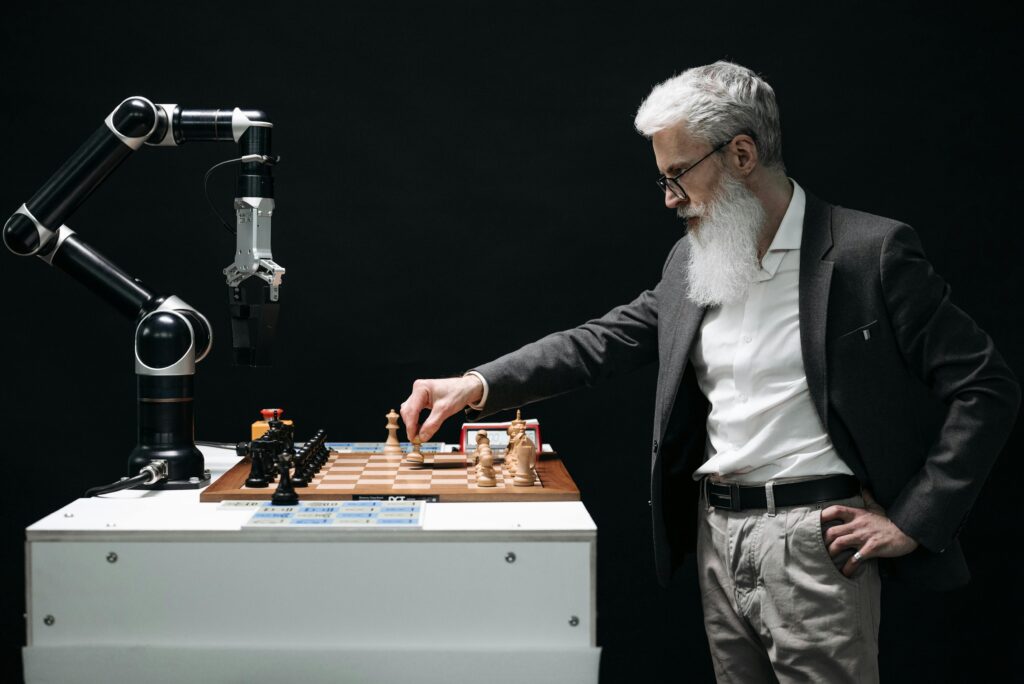 A bearded man engages in a chess game with a robotic arm, highlighting technology and strategy.